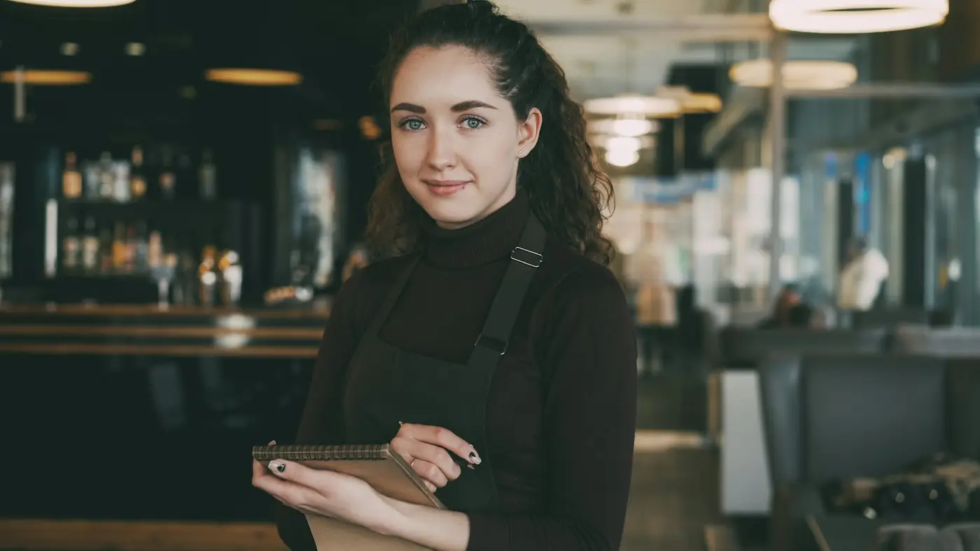A smiling restaurant owner in an apron holding a tablet